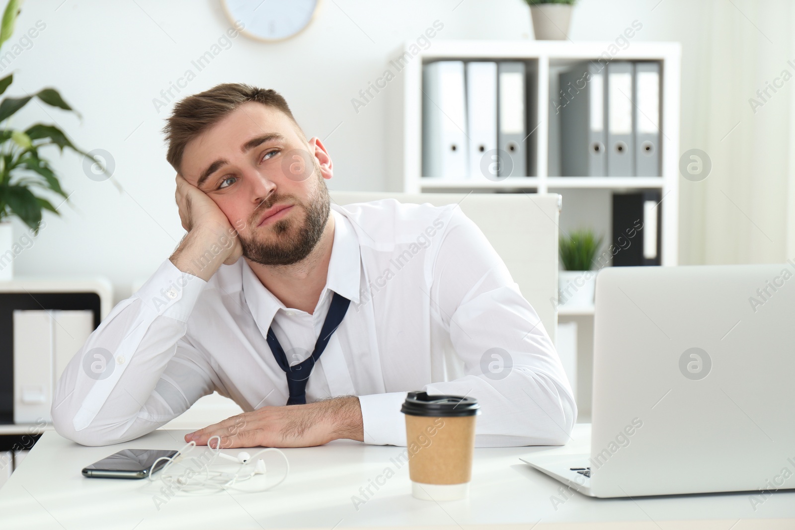 Photo of Lazy young man wasting time at table in office