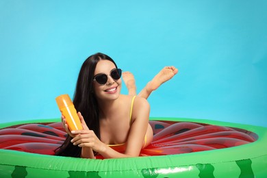 Photo of Young woman with sun protection cream on inflatable mattress against light blue background