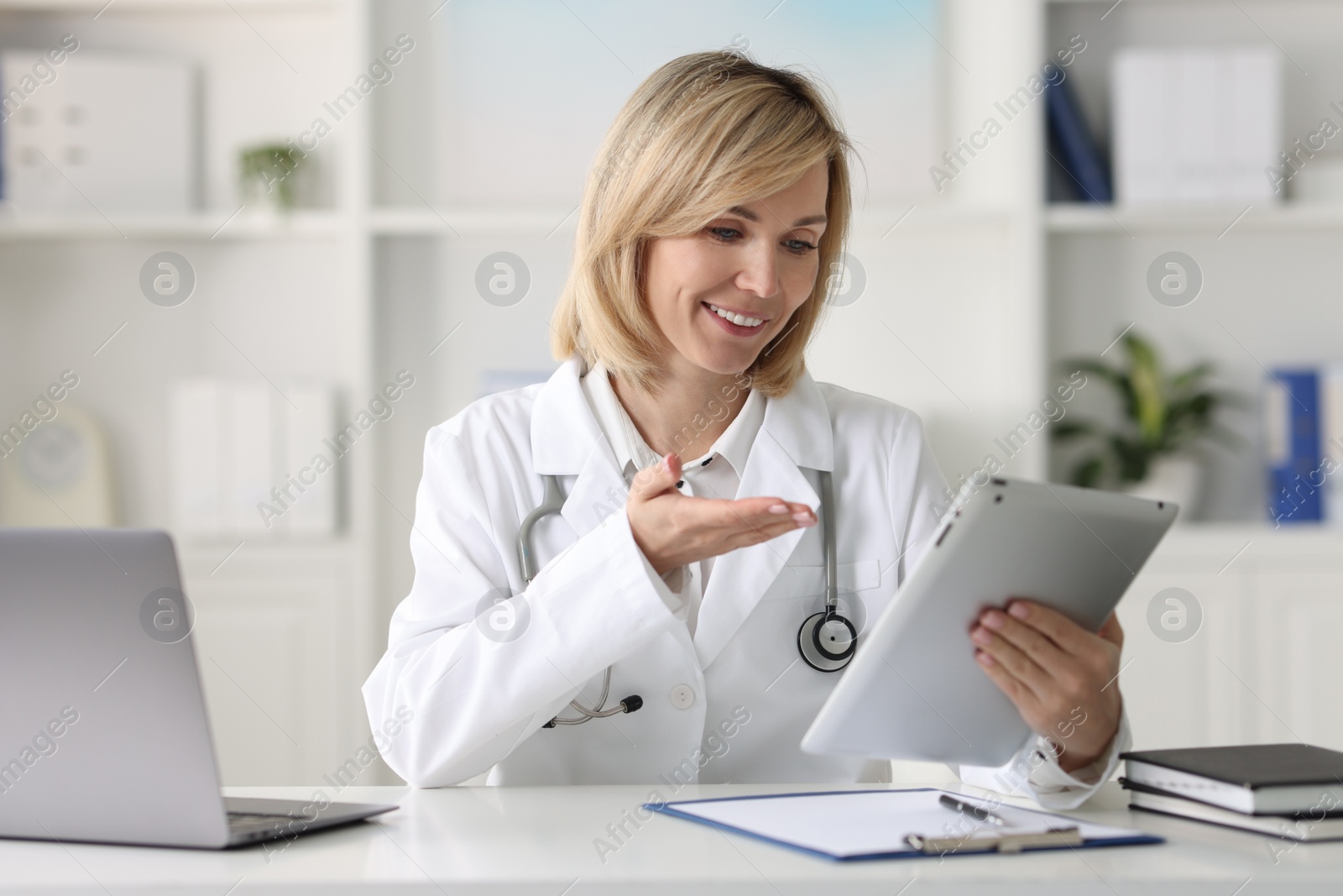 Photo of Smiling doctor with tablet having online consultation at table in office