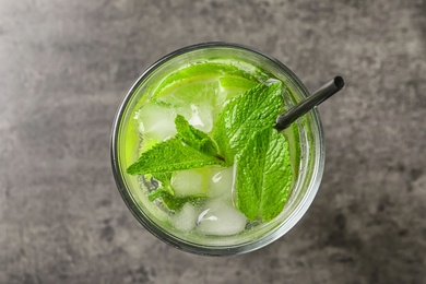 Refreshing beverage with mint and lime in glass on grey background, top view