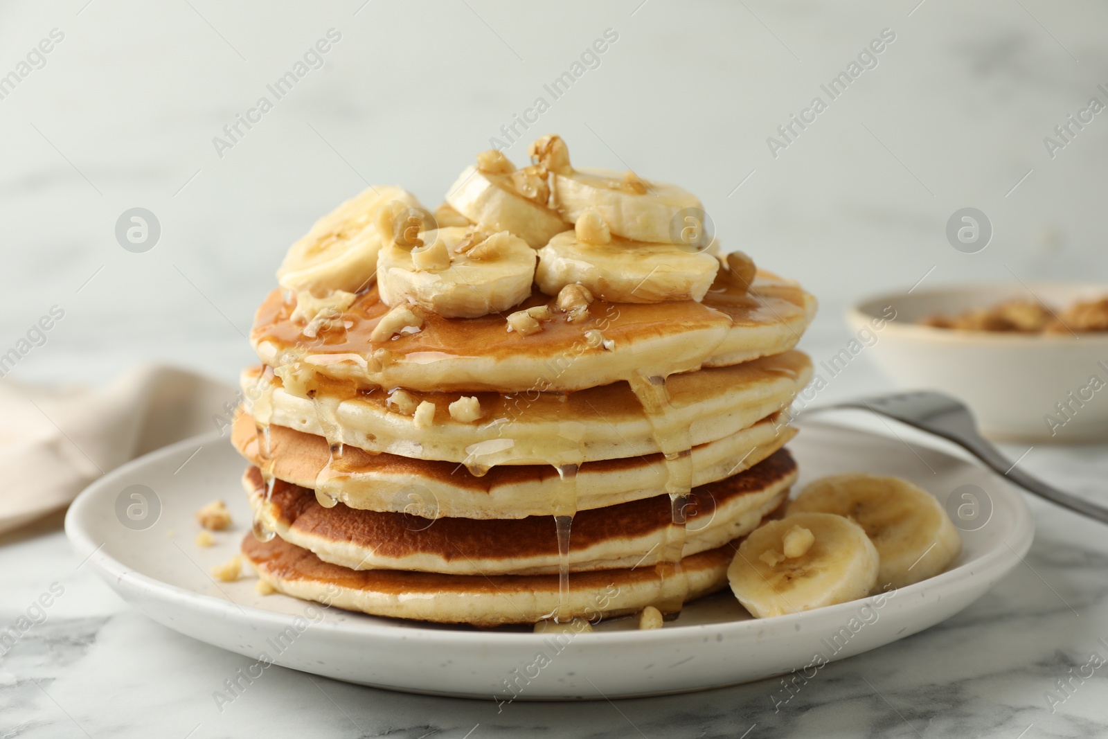 Photo of Delicious pancakes with bananas, walnuts and honey on white marble table, closeup