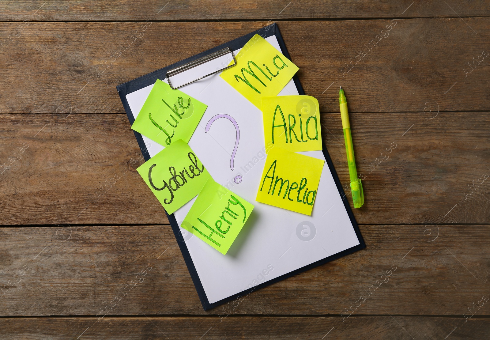 Photo of Paper notes with different baby names, clipboard and pen on wooden table, flat lay