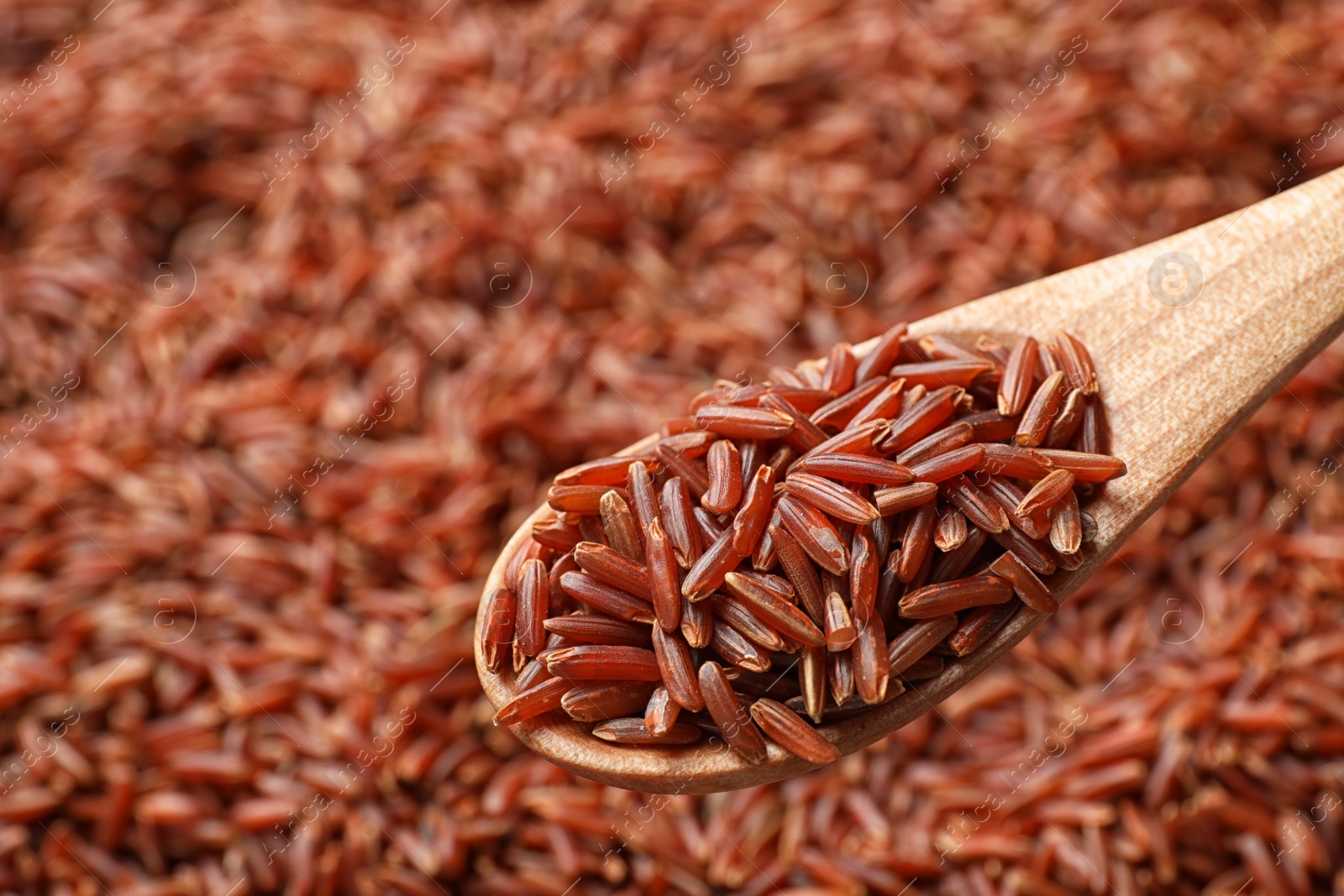 Photo of Wooden spoon with raw brown rice over cereal, closeup