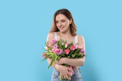 Photo of Happy young woman with bouquet of beautiful tulips on light blue background