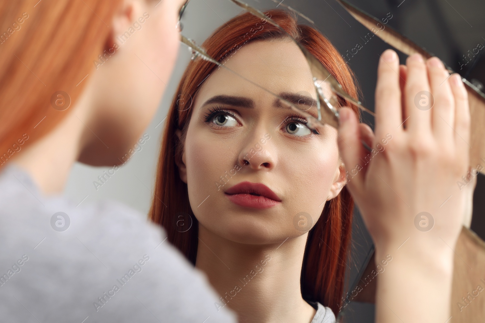 Photo of Sad young woman suffering from mental problems near broken mirror