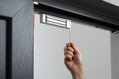 Photo of Man with screwdriver installing electromagnetic door lock indoors, closeup. Home security