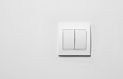 Photo of Modern plastic light switch on white wall, space for text