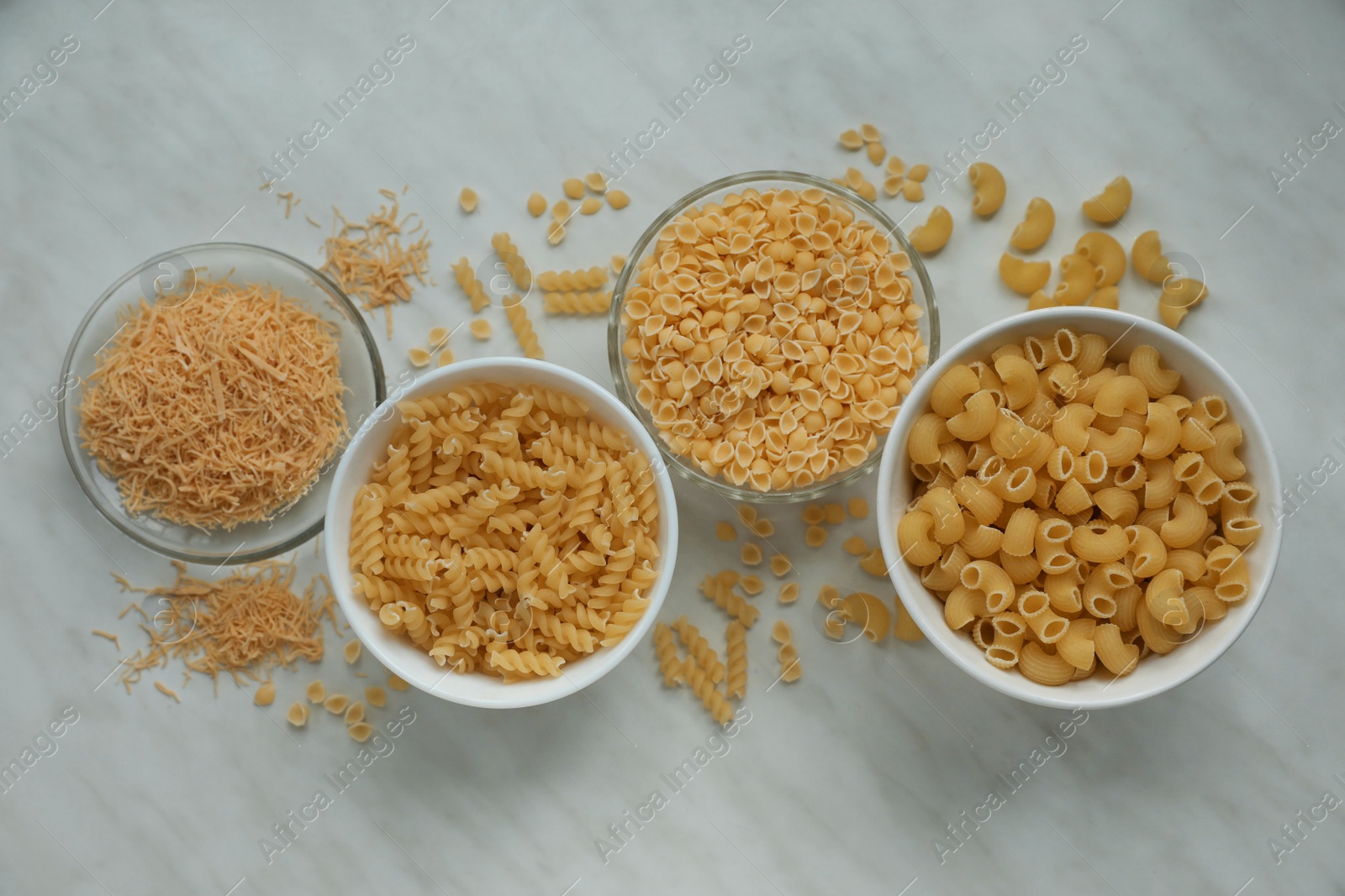 Photo of Different types of pasta on white marble table, flat lay