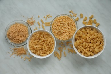 Different types of pasta on white marble table, flat lay