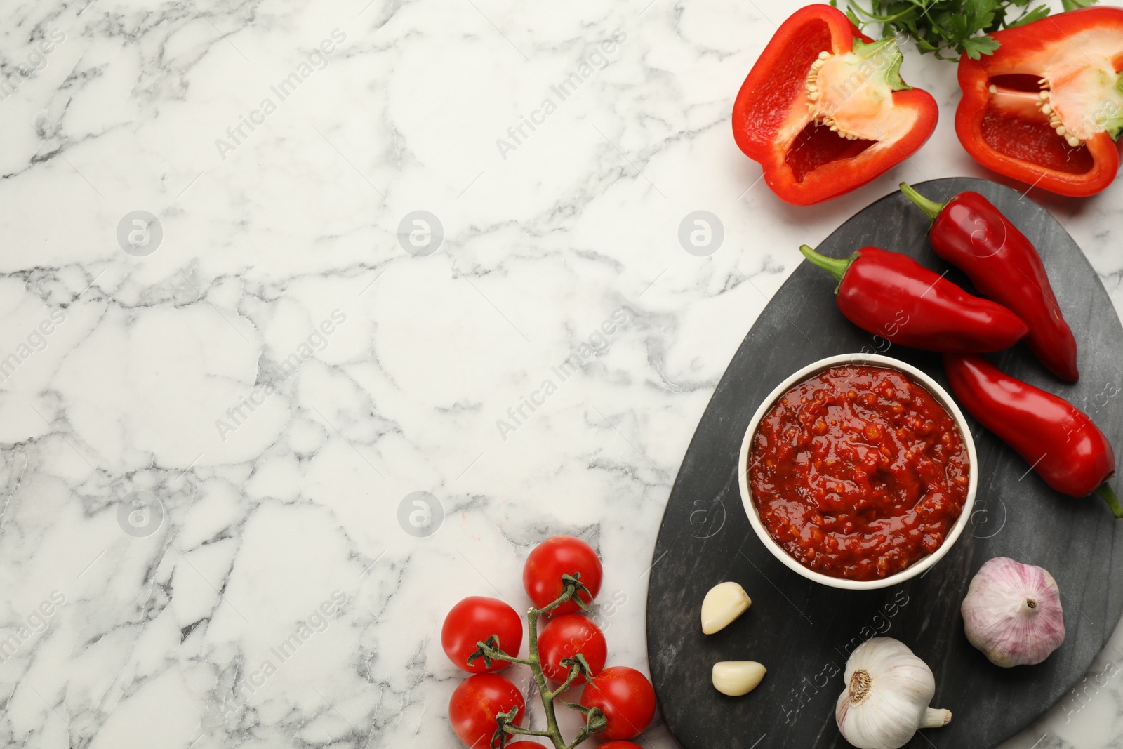 Photo of Delicious adjika sauce in bowl and ingredients on white marble table, flat lay. Space for text