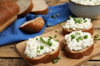 Bread with cottage cheese and green onion on wooden table, closeup