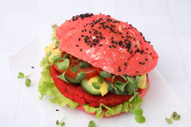 Photo of Tasty pink vegan burger with vegetables, patty and microgreens on white tiled table, closeup