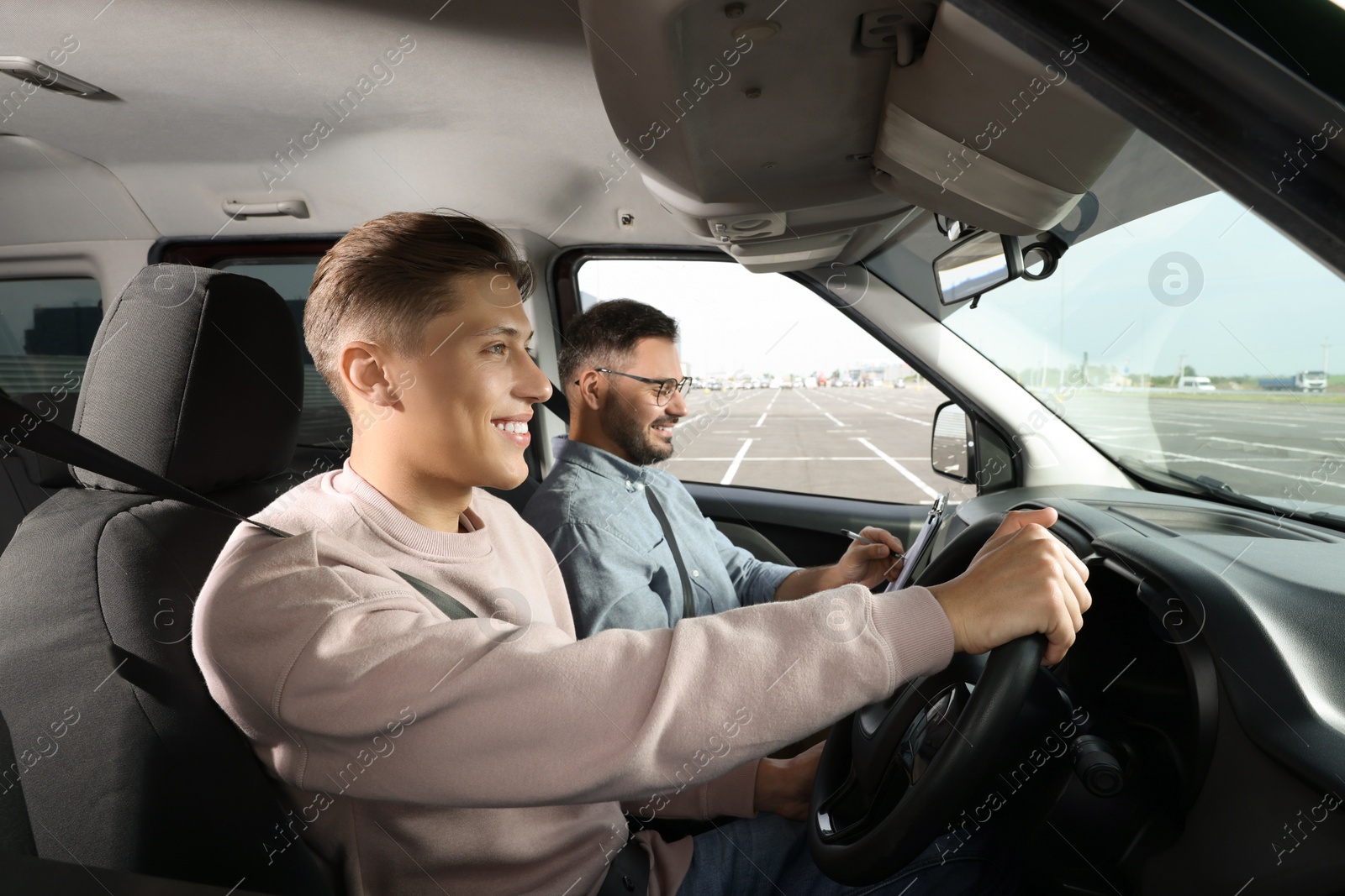 Photo of Driving school. Happy student passing driving test with examiner in car at parking lot