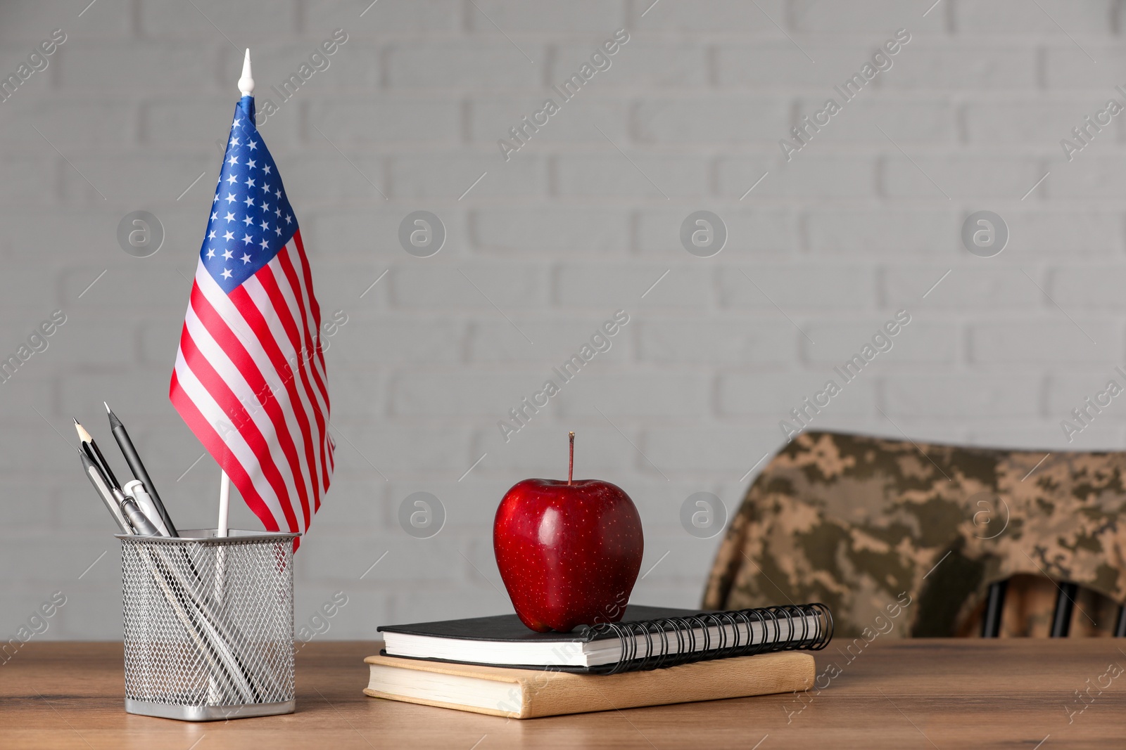 Photo of Notebooks, apple and pen holder with flag of USA on wooden table. Military education
