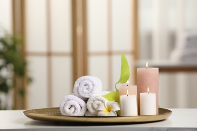 Photo of Spa composition. Burning candles, plumeria flower, green leaves and towels on white table indoors, space for text