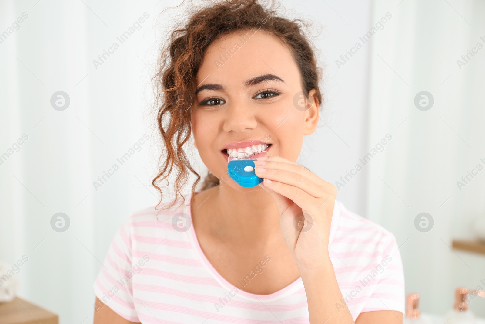 Photo of Young African-American woman using teeth whitening device at home