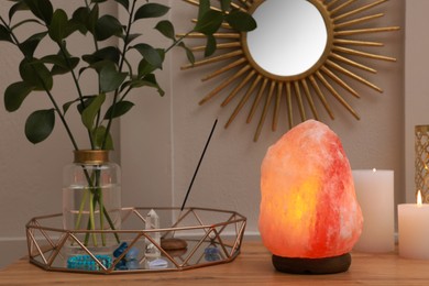 Himalayan salt lamp, candles and crystals on wooden table near white wall indoors
