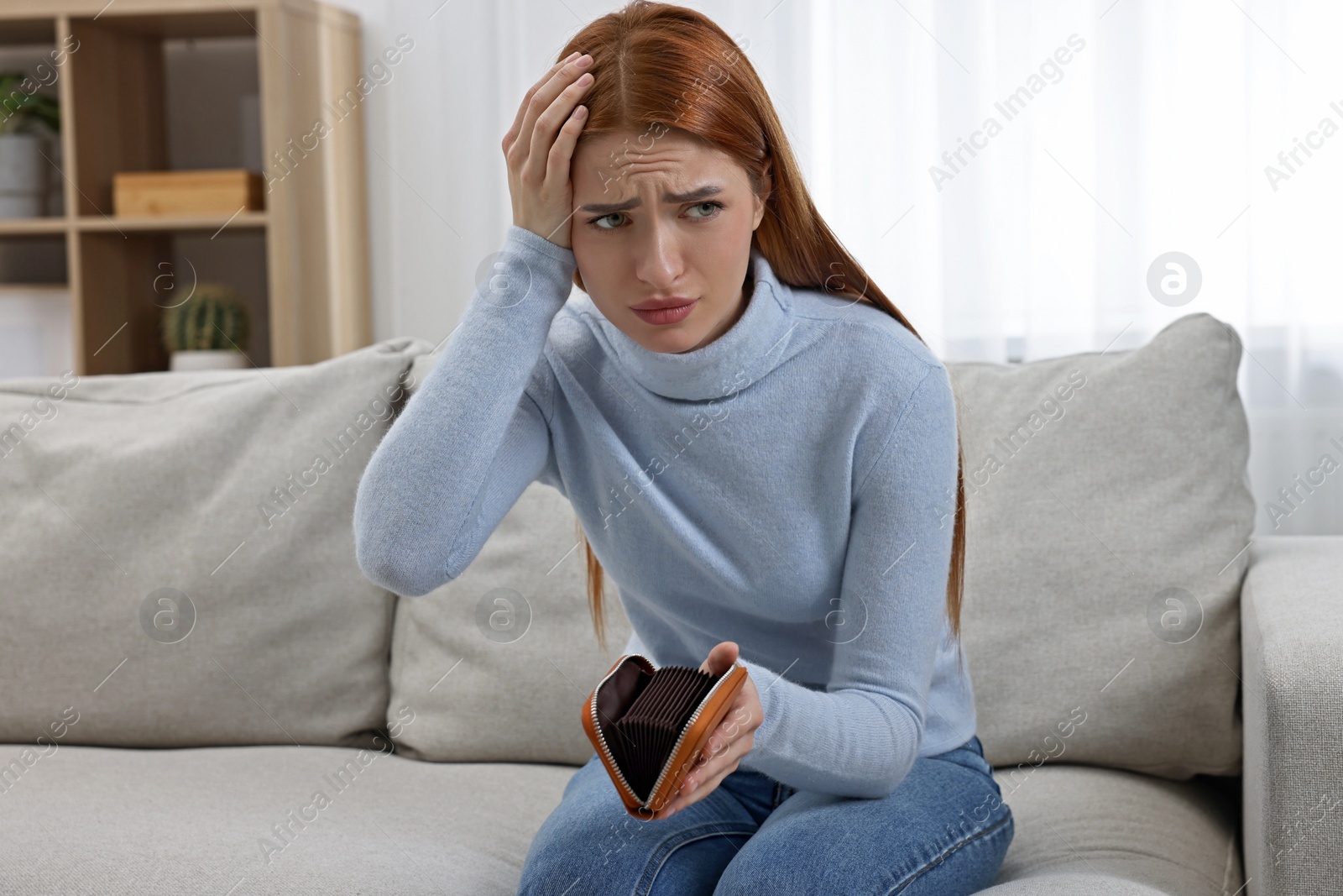 Photo of Upset woman with empty wallet on sofa indoors