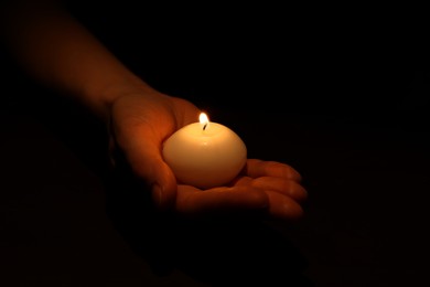 Woman holding burning candle in hand on black background, closeup