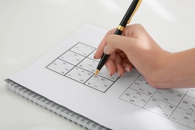 Photo of Woman solving sudoku puzzle at white table, closeup