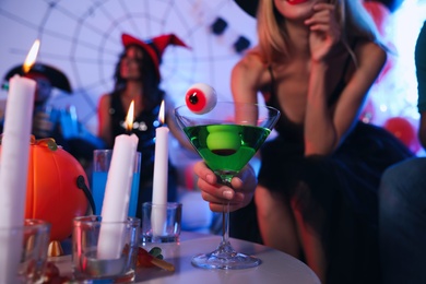 Photo of Woman holding cocktail with jelly eyeballs at Halloween party, closeup