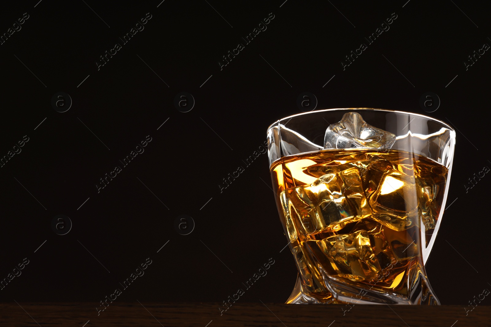 Photo of Whiskey with ice cubes in glass on table against black background. Space for text