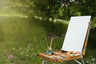 Easel with blank canvas and painting equipment in picturesque countryside