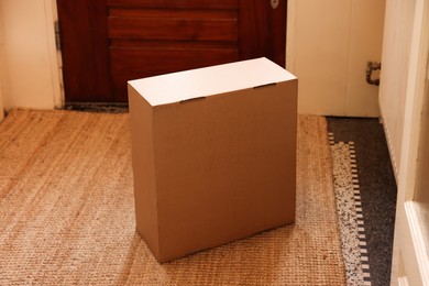 Photo of Delivery service. Cardboard on rug near wooden door indoors