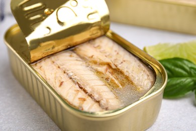 Photo of Open tin can with mackerel fillets on grey table, closeup