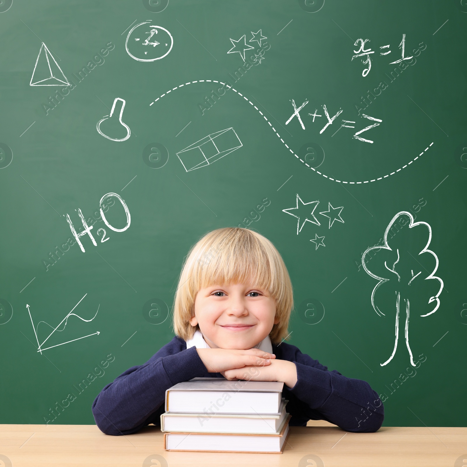 Image of School boy at desk near green chalkboard with drawings and inscriptions