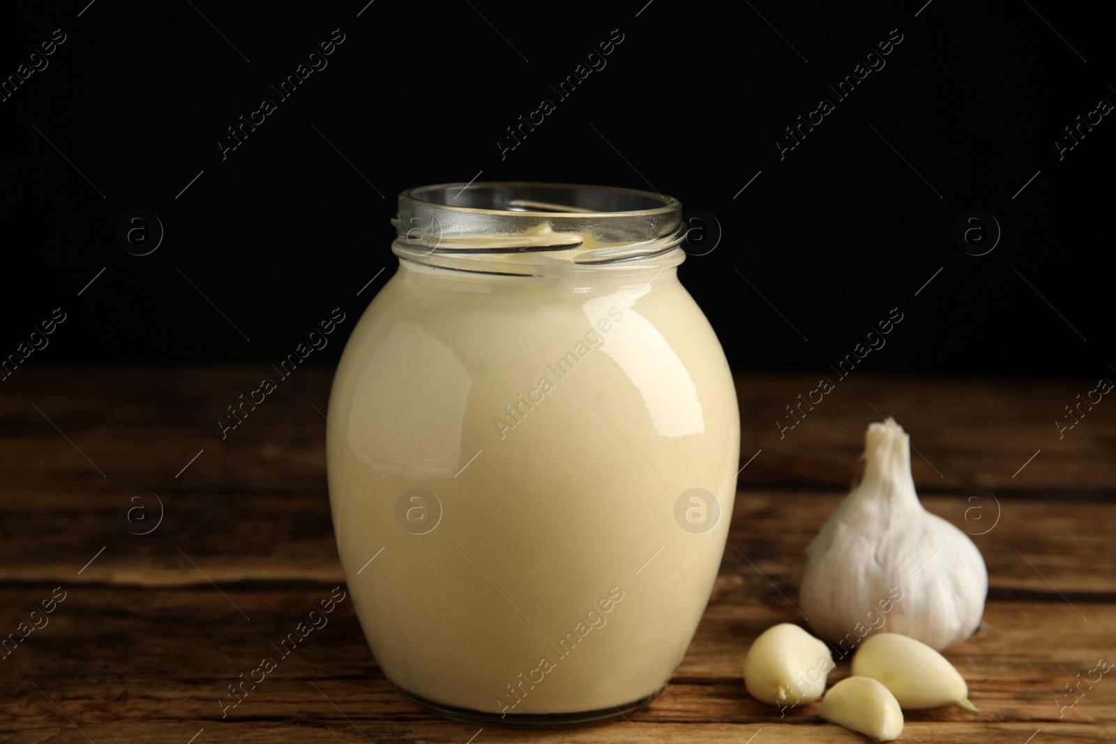 Photo of Jar of delicious mayonnaise and fresh garlic on wooden table