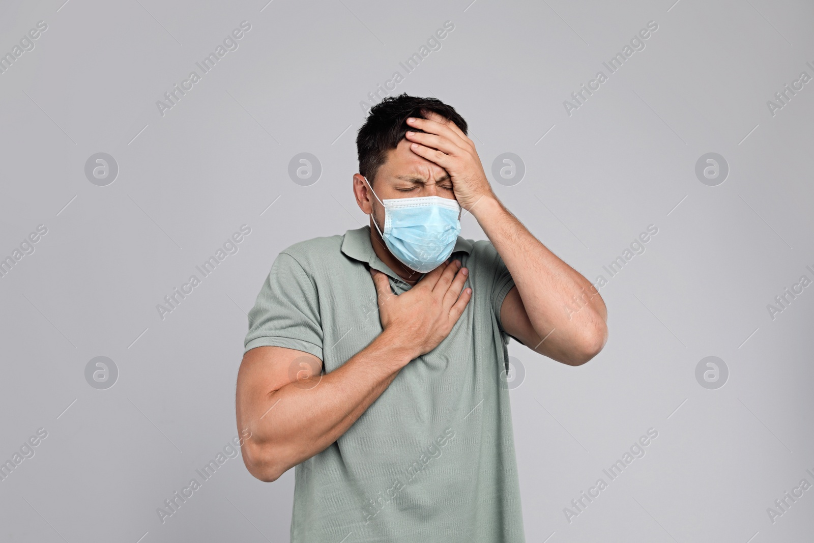 Photo of Man in medical mask suffering from pain during breathing on grey background