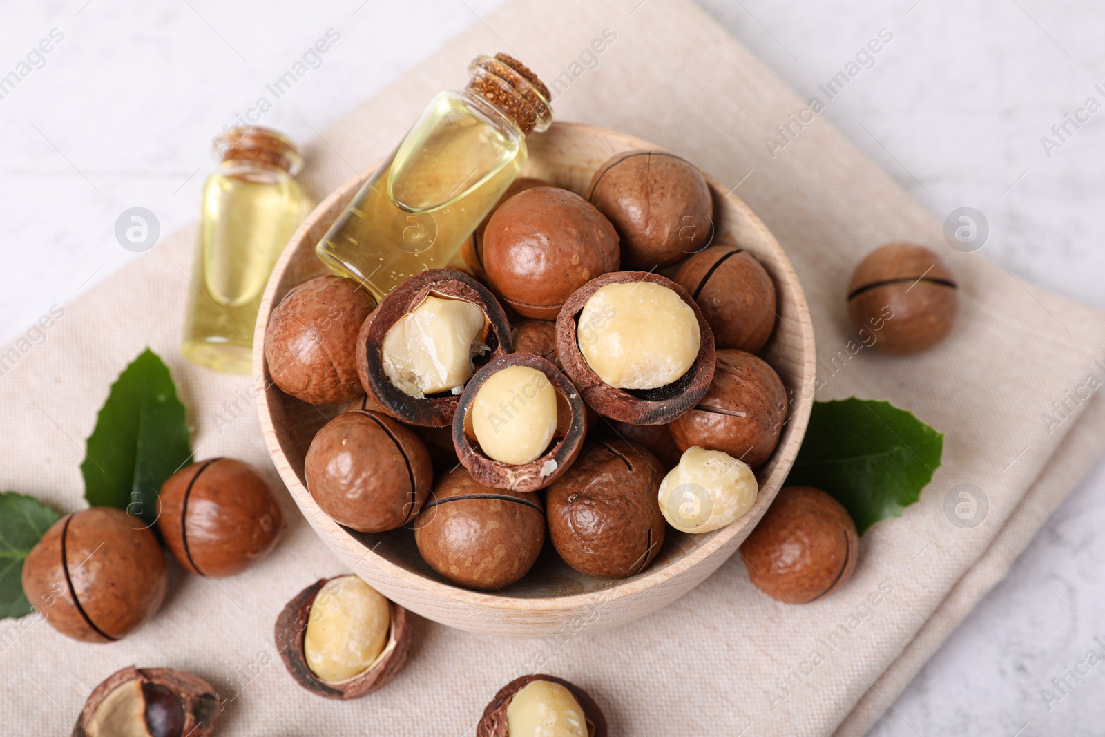 Photo of Bowl with organic Macadamia nuts and natural oil on white textured table, above view