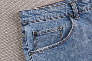 Photo of Stylish light blue jeans on grey fabric, closeup of inset pocket