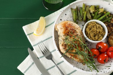 Photo of Tasty chicken, vegetables with tarragon and pesto sauce served on green wooden table, flat lay. Space for text