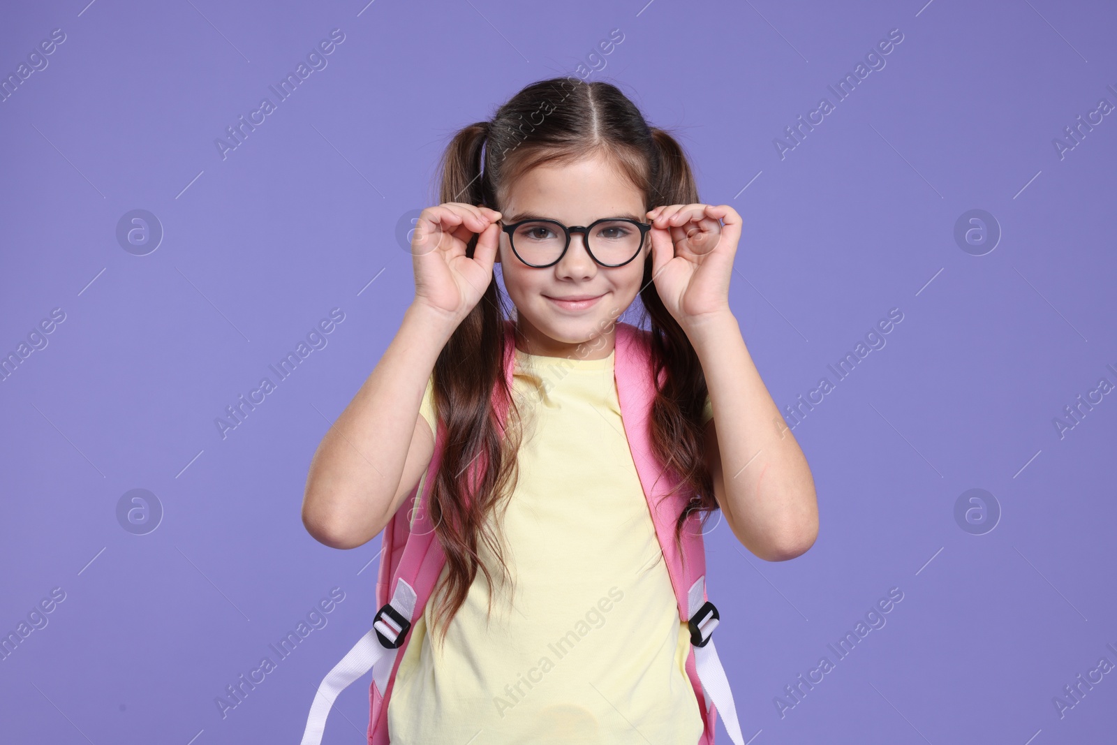 Photo of Cute schoolgirl in glasses with backpack on violet background