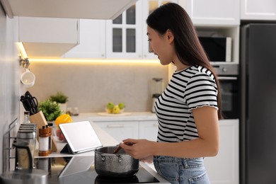 Photo of Woman looking at recipe on tablet while cooking in kitchen