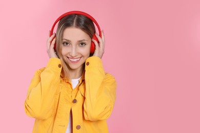 Teenage girl listening to music with red headphones on pink background. Space for text