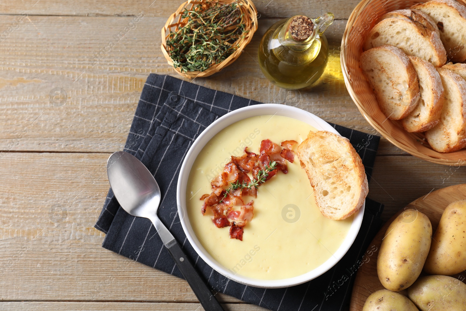 Photo of Tasty potato soup with bacon in bowl served on wooden table, flat lay