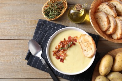 Tasty potato soup with bacon in bowl served on wooden table, flat lay