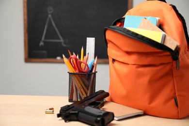 Gun, bullets and school stationery on wooden table near blackboard indoors, space for text