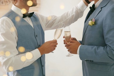 Photo of Newlywed gay couple with glasses of champagne at home, closeup