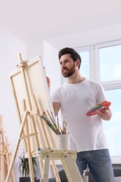 Photo of Man painting in studio. Using easel to hold canvas