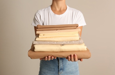 Woman holding stack of clean bed linens on beige background