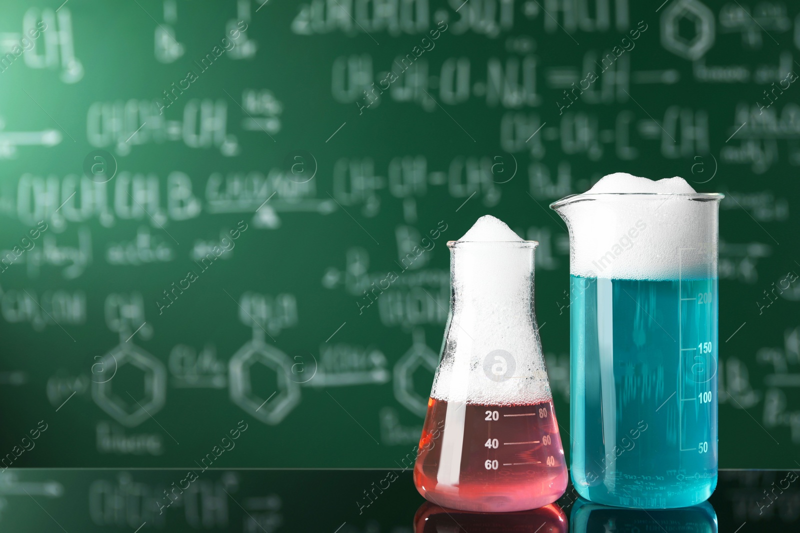 Photo of Laboratory glassware with colorful liquids on glass table, space for text. Chemical reaction