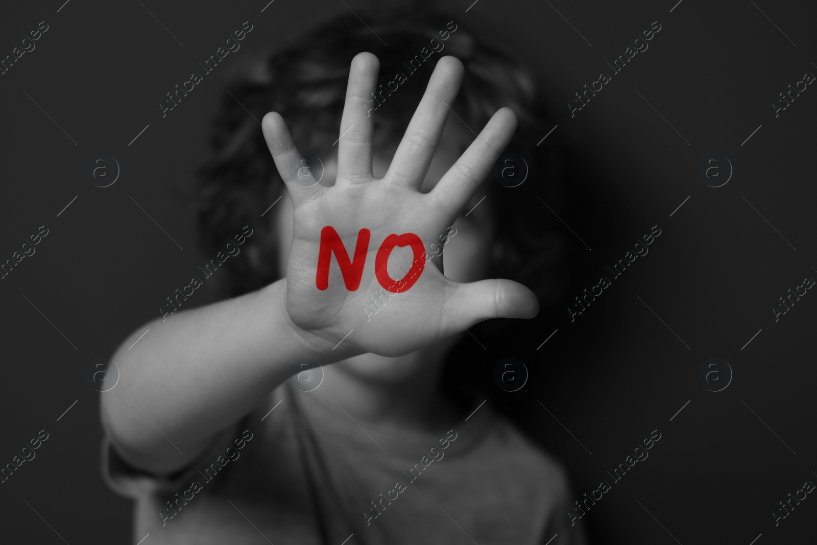 Image of Child abuse. Boy making stop gesture near dark wall, black and white effect. No written on his hand