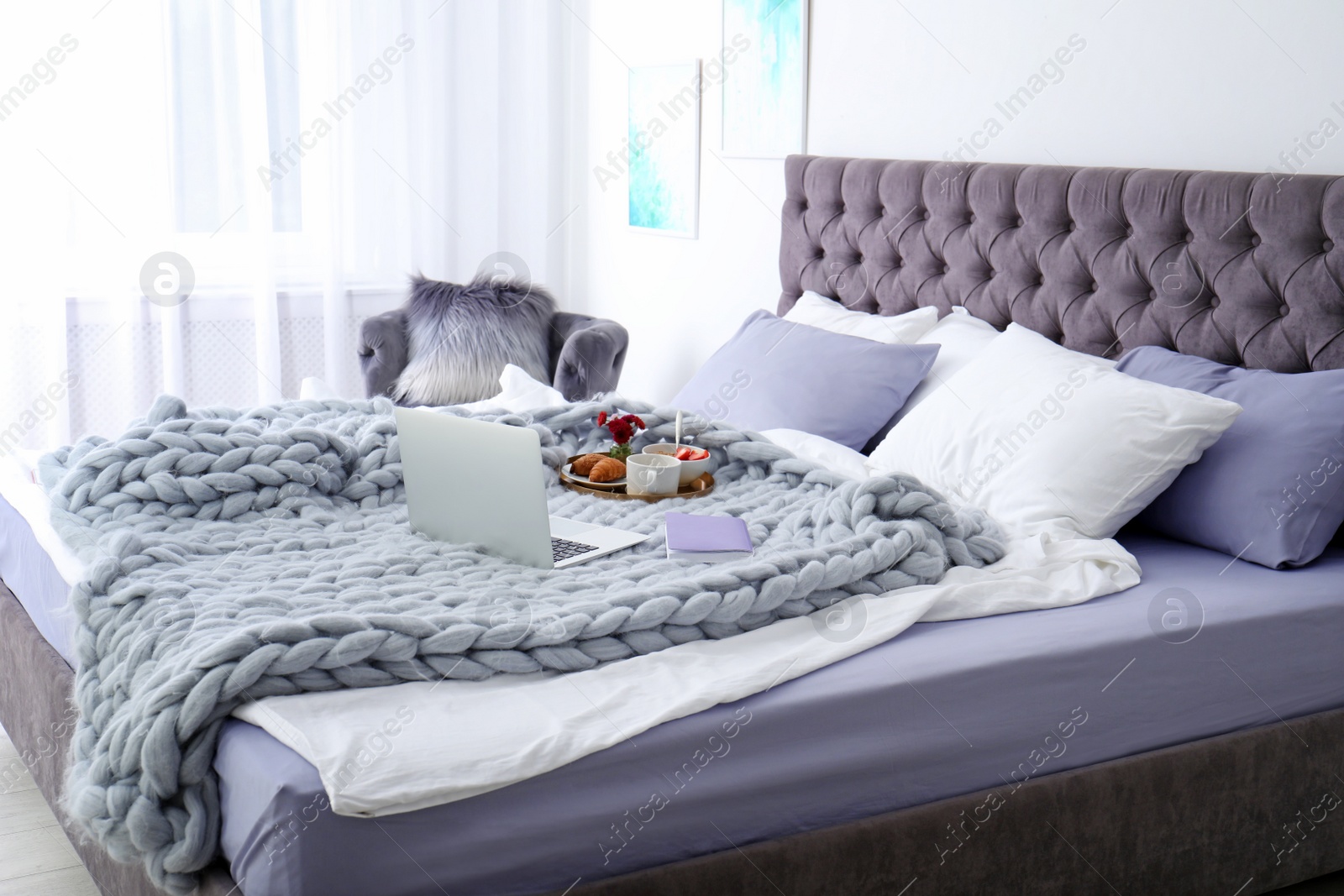 Photo of Laptop, notebook and tray with breakfast on bed in stylish room interior