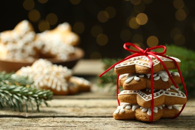 Photo of Tasty Christmas cookies with icing on wooden table against blurred lights. Space for text