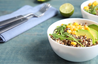 Healthy quinoa salad with vegetables in bowl on wooden table. Space for text