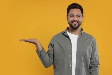 Photo of Special promotion. Smiling man holding something on orange background. Space for text